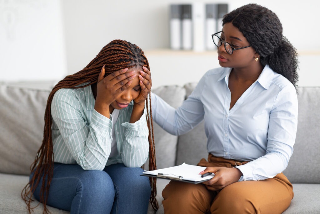 Upset black lady with nervous breakdown consulting psychologist, having session with counselor at clinic.